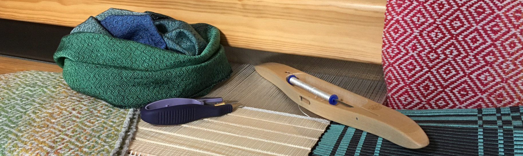 Banner image showing handwoven textiles and weaving tools on top of an in-progress project in the loom.