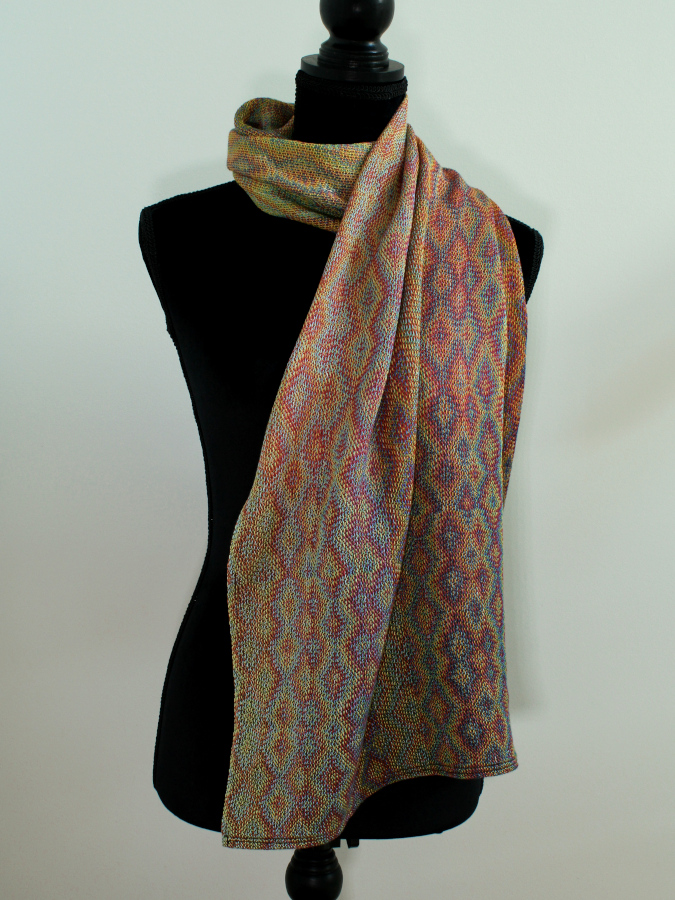 A colorful scarf with complex iridescent diamond patterns, wrapped around the neck of a black sewing mannequin.