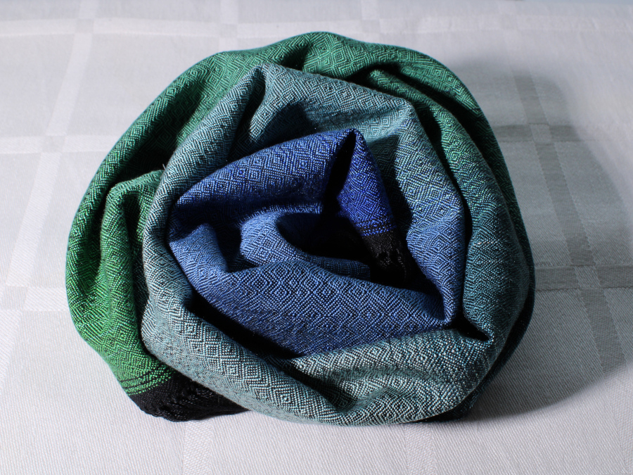 A scarf rolled up in a bun. The fabric is a blue-green gradient with small irregular diamond patterns in black.
