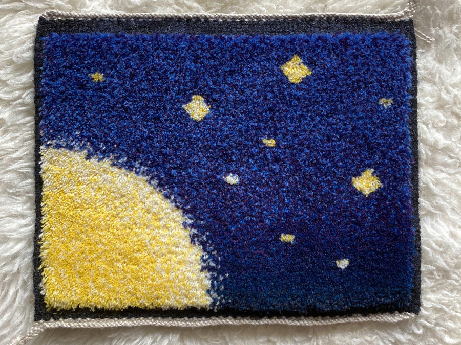 Miniature pile carpet representing an abstract space scene, with a yellow quarter-sun in the bottom-left corner, a few stars, and a gradient blue-purple sky.